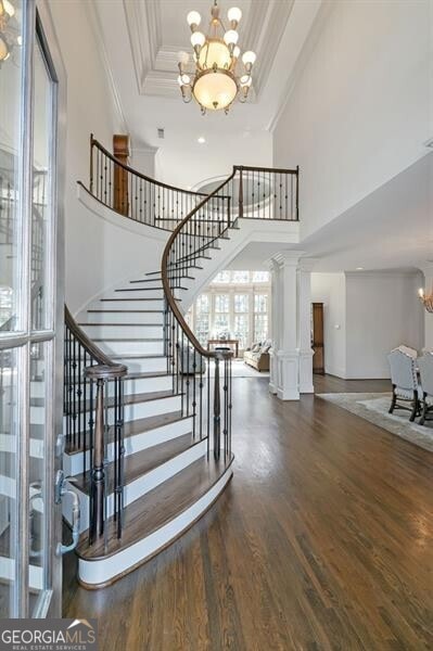 stairway featuring ornate columns, wood-type flooring, a towering ceiling, a notable chandelier, and ornamental molding