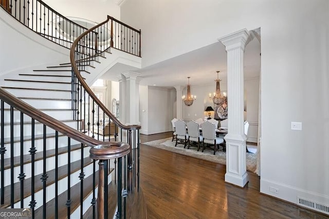 stairs with decorative columns, a chandelier, wood-type flooring, and a towering ceiling