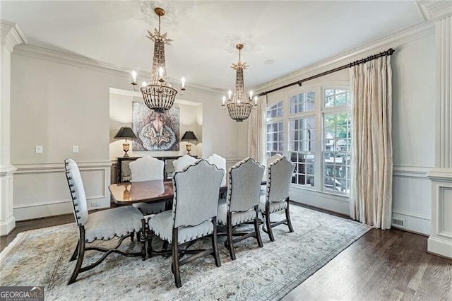 dining area with dark wood-type flooring, a notable chandelier, crown molding, and decorative columns