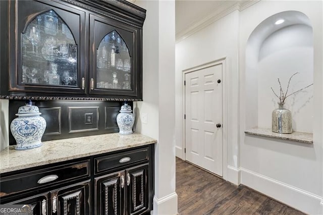 bar featuring ornamental molding, dark wood-type flooring, and light stone counters