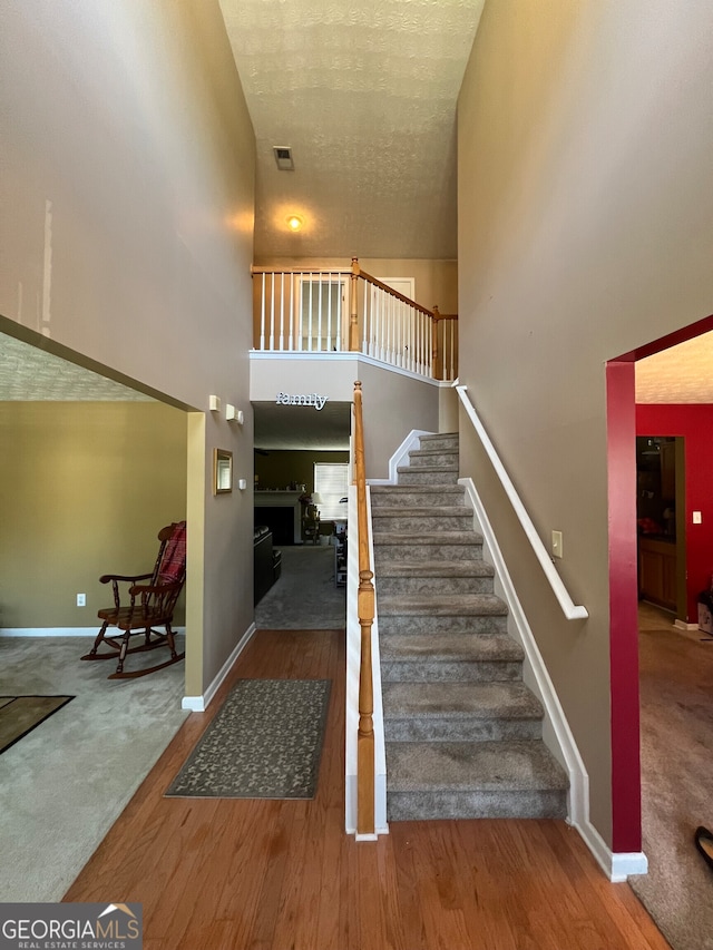 stairway featuring a fireplace, hardwood / wood-style flooring, and high vaulted ceiling