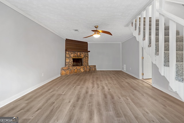 unfurnished living room with ceiling fan, a textured ceiling, light hardwood / wood-style flooring, a fireplace, and crown molding