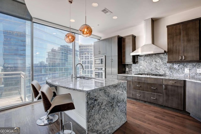 kitchen featuring dark hardwood / wood-style flooring, appliances with stainless steel finishes, wall chimney range hood, and plenty of natural light