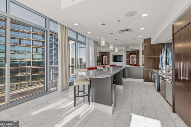 kitchen featuring hanging light fixtures, a kitchen island, a kitchen breakfast bar, light stone countertops, and floor to ceiling windows