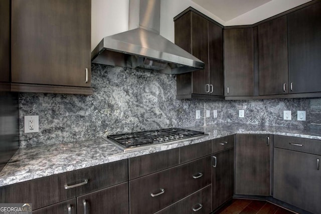 kitchen with backsplash, wall chimney exhaust hood, stainless steel gas stovetop, dark wood-type flooring, and light stone counters