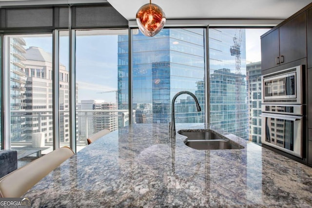 kitchen with stainless steel microwave, floor to ceiling windows, stone counters, dark brown cabinetry, and sink