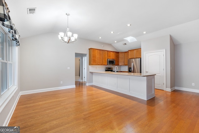 kitchen with lofted ceiling with skylight, light wood-type flooring, kitchen peninsula, and stainless steel appliances