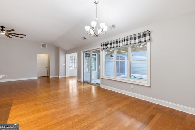 empty room featuring hardwood / wood-style floors, ceiling fan with notable chandelier, and vaulted ceiling