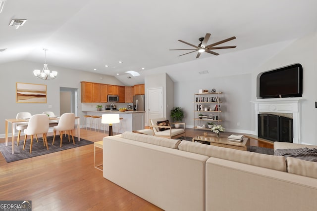 living room with ceiling fan with notable chandelier, light hardwood / wood-style flooring, and lofted ceiling