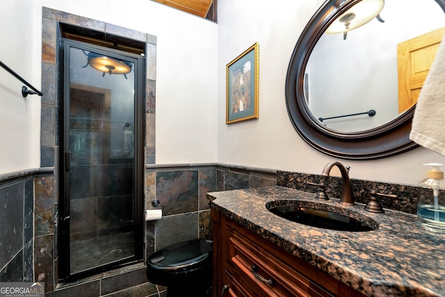 bathroom featuring toilet, vanity, a shower with door, and tile walls