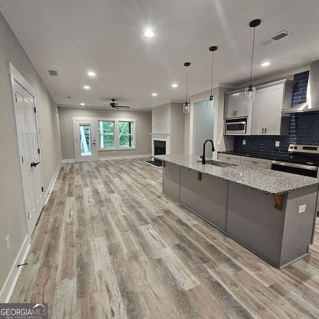 kitchen featuring light stone countertops, wall chimney range hood, sink, light hardwood / wood-style floors, and stainless steel appliances