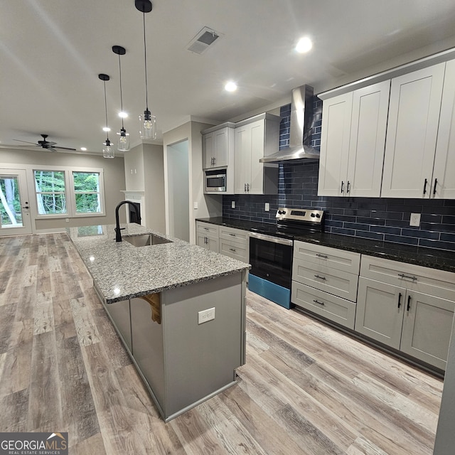 kitchen featuring a kitchen island with sink, wall chimney range hood, light hardwood / wood-style flooring, sink, and appliances with stainless steel finishes