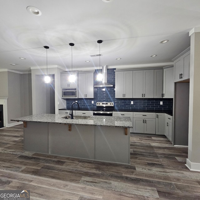 kitchen featuring wall chimney range hood, an island with sink, light stone countertops, sink, and stainless steel appliances