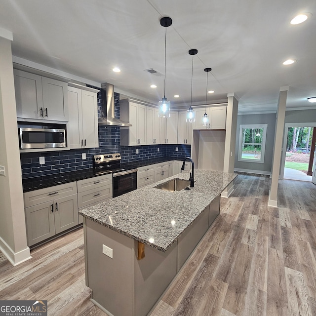 kitchen with wall chimney range hood, a center island with sink, light hardwood / wood-style flooring, stainless steel appliances, and sink