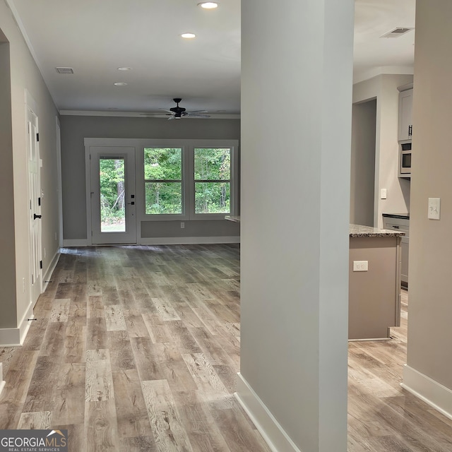 corridor with light hardwood / wood-style floors and ornamental molding