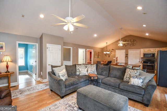 living room featuring ceiling fan with notable chandelier, light wood-type flooring, and lofted ceiling