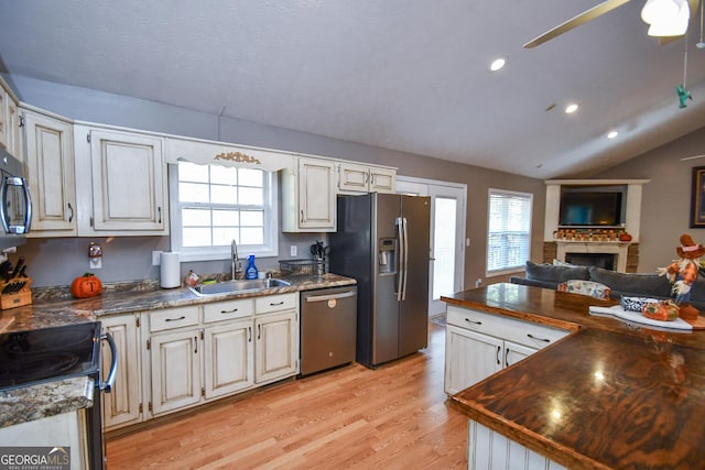 kitchen featuring stainless steel appliances, light hardwood / wood-style floors, sink, a fireplace, and lofted ceiling