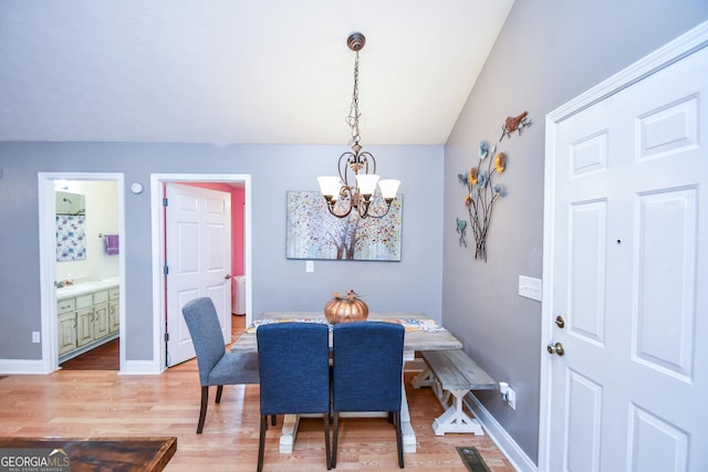 dining area with sink, wood-type flooring, a chandelier, and vaulted ceiling