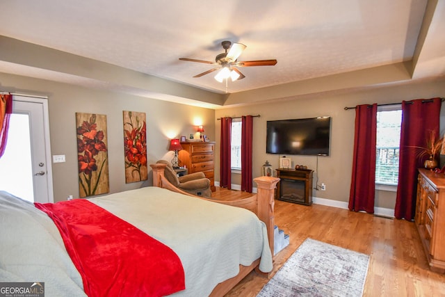 bedroom with light hardwood / wood-style floors, multiple windows, ceiling fan, and a tray ceiling