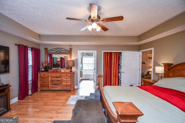 bedroom featuring ceiling fan, a textured ceiling, light hardwood / wood-style flooring, connected bathroom, and a closet