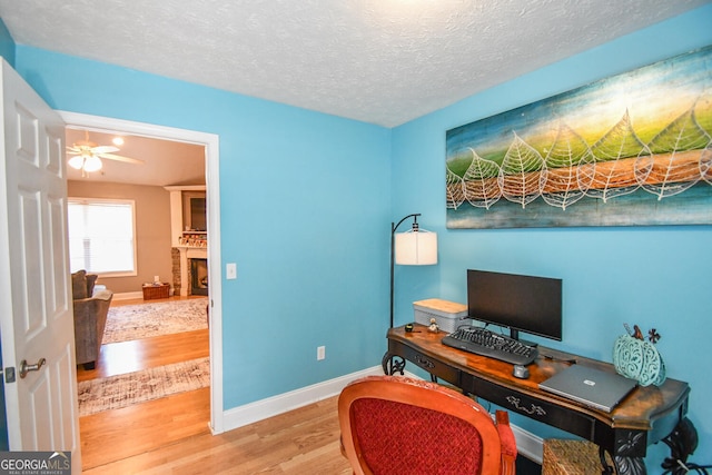 office area featuring a textured ceiling, a brick fireplace, wood-type flooring, and ceiling fan