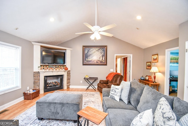 living room with a stone fireplace, light wood-type flooring, lofted ceiling, and ceiling fan