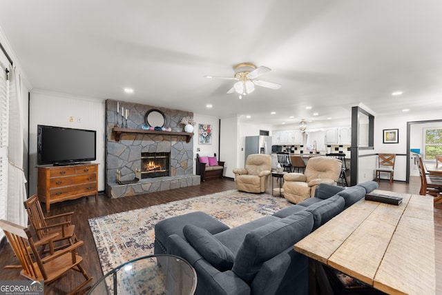 living room featuring a stone fireplace, dark wood-type flooring, and ceiling fan