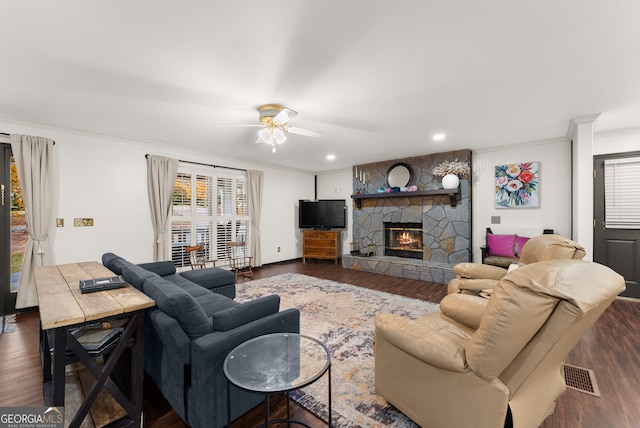 living room featuring dark wood-type flooring, ornamental molding, a stone fireplace, and ceiling fan