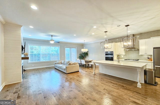 living room featuring ceiling fan with notable chandelier, light wood-type flooring, and crown molding