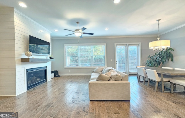 living room featuring ceiling fan, hardwood / wood-style floors, ornamental molding, and a fireplace