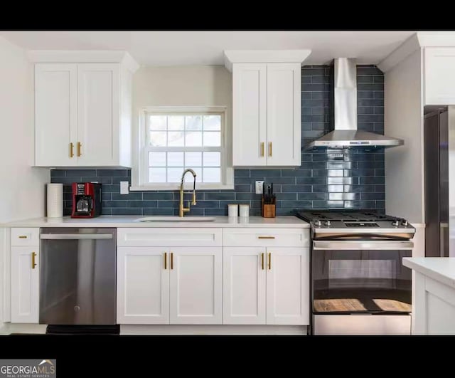 kitchen with wall chimney range hood, white cabinetry, stainless steel appliances, and sink