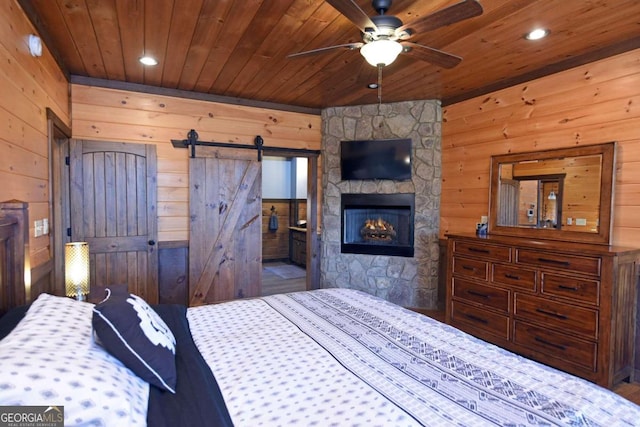 bedroom featuring a barn door, wooden walls, ceiling fan, and wooden ceiling