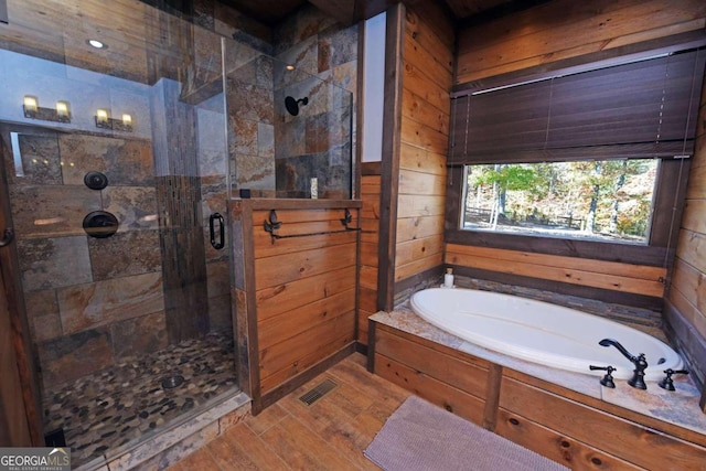 bathroom with wood-type flooring, independent shower and bath, and wooden walls