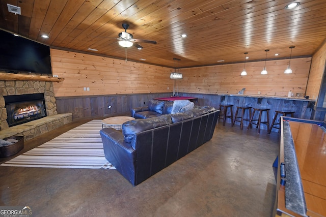 living room with ceiling fan, wood walls, a stone fireplace, and wood ceiling