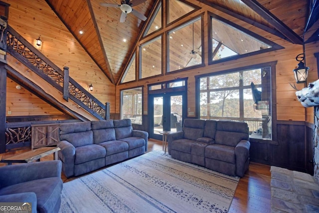 living room with ceiling fan, french doors, high vaulted ceiling, wood walls, and wood-type flooring