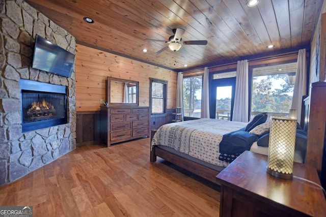 bedroom featuring wooden ceiling, wooden walls, ceiling fan, a fireplace, and wood-type flooring