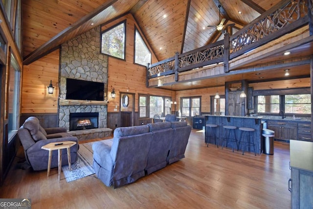 living room featuring wood ceiling, wooden walls, high vaulted ceiling, hardwood / wood-style floors, and a stone fireplace