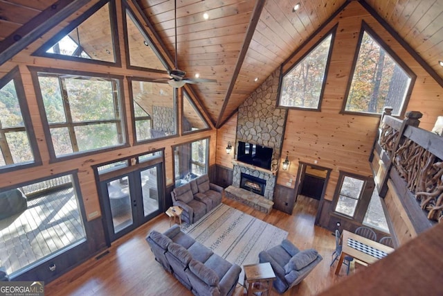 living room featuring hardwood / wood-style floors, a stone fireplace, wooden walls, ceiling fan, and wood ceiling