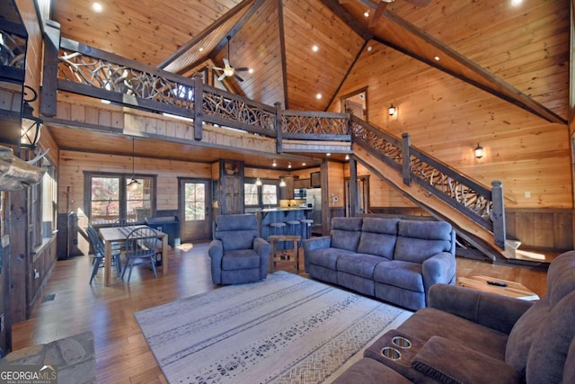 living room with ceiling fan, wood-type flooring, high vaulted ceiling, beamed ceiling, and wood walls