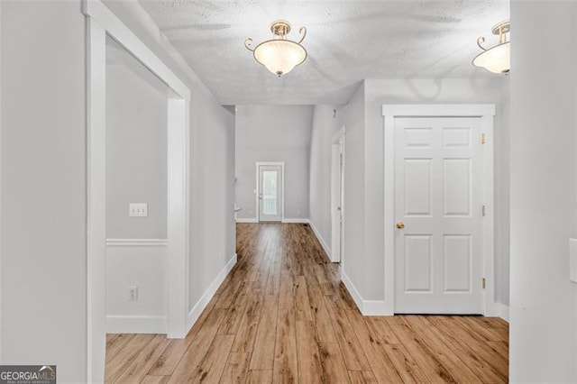 hall with a textured ceiling and light wood-type flooring