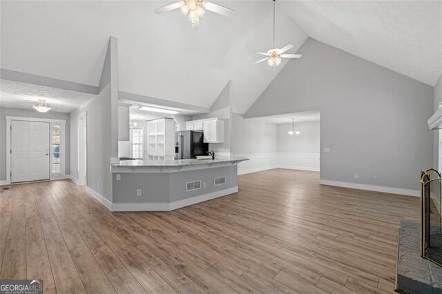 unfurnished living room with hardwood / wood-style floors, a fireplace, high vaulted ceiling, and ceiling fan with notable chandelier