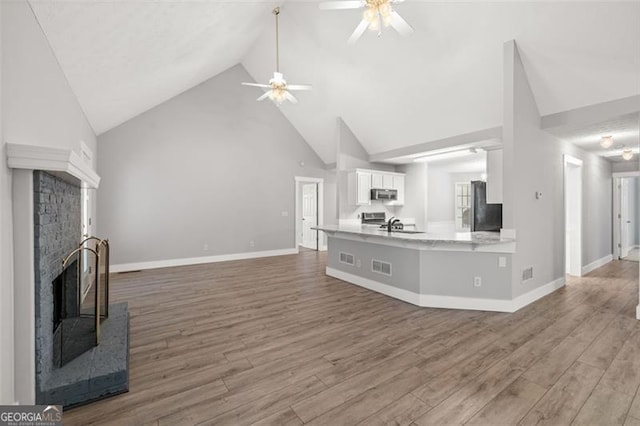 living room featuring ceiling fan, high vaulted ceiling, wood-type flooring, and a fireplace