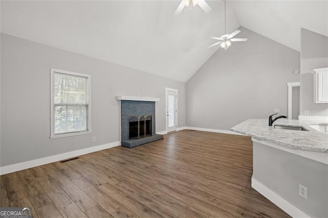 unfurnished living room with dark wood-type flooring, sink, a fireplace, high vaulted ceiling, and ceiling fan