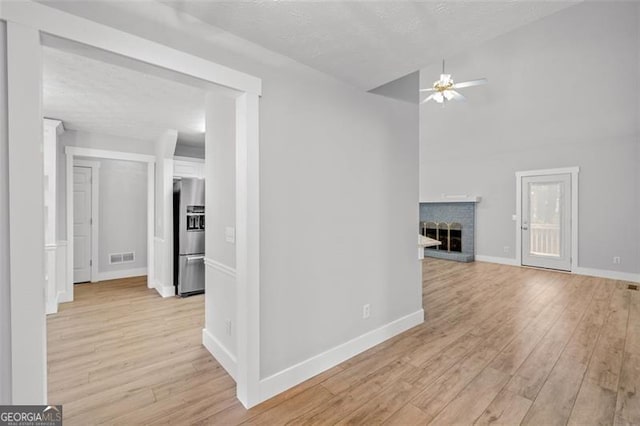 interior space with a brick fireplace, a textured ceiling, light wood-type flooring, and ceiling fan