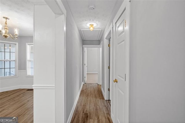 corridor featuring a textured ceiling, hardwood / wood-style flooring, and a chandelier