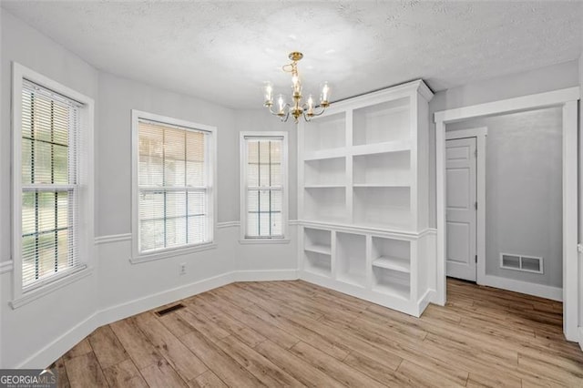 unfurnished dining area featuring a chandelier, light hardwood / wood-style flooring, and a textured ceiling