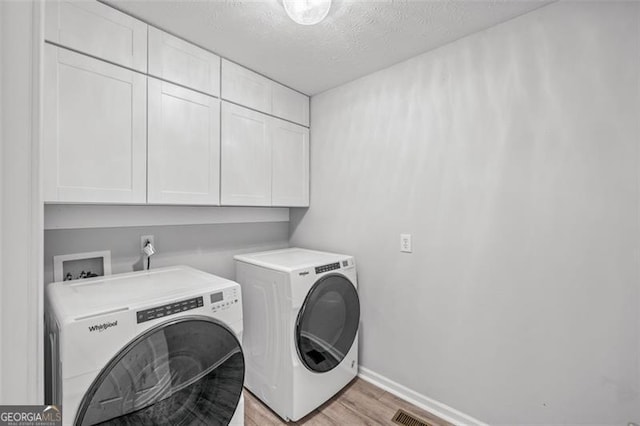 clothes washing area with cabinets, a textured ceiling, separate washer and dryer, and light wood-type flooring