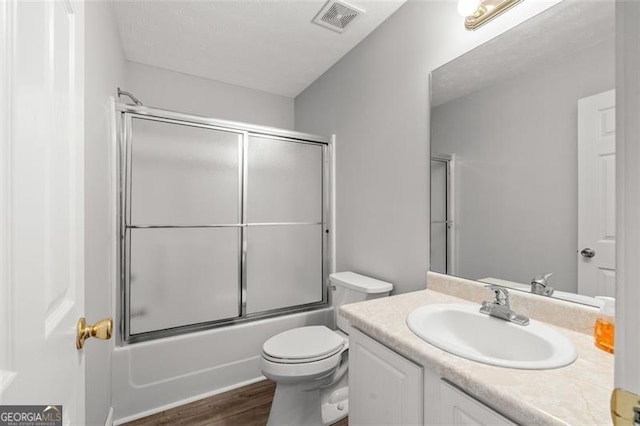 full bathroom with vanity, hardwood / wood-style floors, shower / bath combination with glass door, and toilet