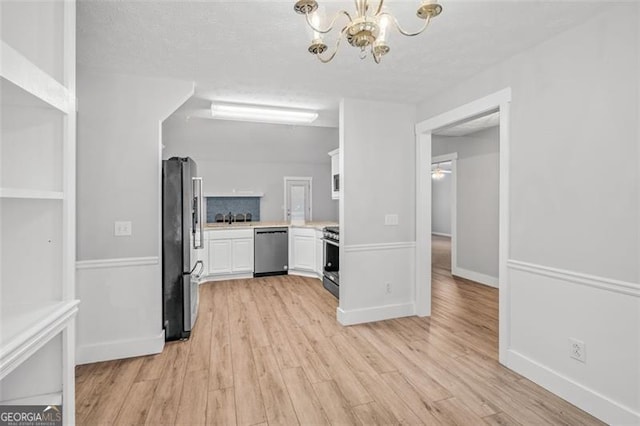 interior space featuring stainless steel appliances, a notable chandelier, pendant lighting, light wood-type flooring, and white cabinetry