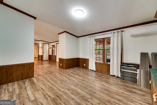 spare room with wooden walls, a wall mounted AC, ornamental molding, a textured ceiling, and light hardwood / wood-style flooring